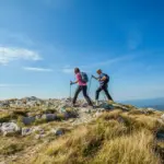 couple-hiking-nanos-plateau-slovenia-against-blue-sky