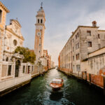 Venice, Italy - October 2022: Typical Venetian boat as it sails past the church of San Giorgio dei Greci with its typical leaning bell tower