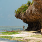 Tourist enjoying the stunning scenery of a secluded beach in zanzibar, tanzania, with a rocky cliff providing shade