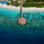 Aerial view of a tropical island resort with turquoise waters, sandy beach, and lush greenery, showcasing a serene vacation paradise.